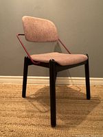 Three-quarter front view of chair showing black wooden legs, red metal frame, beige upholstery