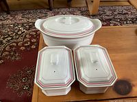 Three Mitterteich casserole dishes including two rectangular and one oval dishes with lids on wooden table and carpet background.