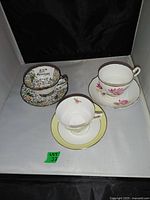 Three English teacups with their saucers in a white display box with black background. Each teacup set has a distinct floral pattern and design.