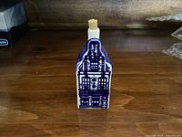 Front view of a blue and white Delft house ceramic bottle with cork stopper showing detailed window and door painting.