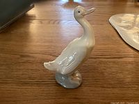 Front-side view of glossy white NAO duck porcelain figurine, showing detailed feathers and blue water base