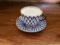 Full view of espresso cup on saucer showing cobalt blue net pattern with gold accents and scalloped gold rim on cup