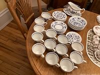 Overall view of 13 cups, 8 saucers, cereal bowls, bread plates, and gravy boat laid out on a wooden table