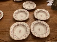 Five rimmed bowls with a pink floral rose pattern, arranged on a table.