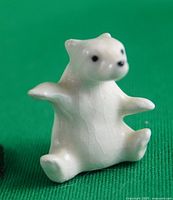 Front view of miniature ceramic polar bear figurine sitting upright with arms raised on green background.