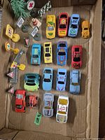 Photo showing 17 die-cast toy cars of various colors and styles along with 12 small plastic traffic signs and accessories arranged inside a cardboard box.