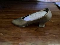 Side view of antique metal shoe pin cushion showing the full shoe shape, gold-colored metal surface, and fabric cushion insert inside.