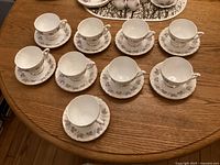 Nine cups and saucers arranged on a wooden table showing all pieces in the set