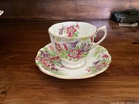 Cup and saucer set in floral Columbine pattern by Royal Albert on wooden table showing side profile of cup with handle and saucer underneath.