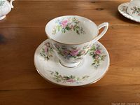 Cup and saucer displayed on wooden table, showing floral pattern and gold trim on cup