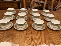 Twelve cups paired with twelve matching saucers arranged on a wooden table, showing the design and quantity.