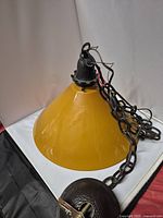 Side view of vintage glass hanging lamp showing mustard yellow conical shade and black mounting chain and wiring.