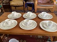 Full overview of 6 place settings on wooden table showing cups, saucers, and plates arranged in sets