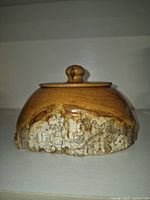 Front and side views of small wooden pot showing smooth wood finish and natural bark on lower half, topped with flat lid with knob.