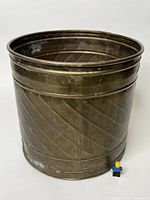 Front angled view of a pressed brass bucket showing diagonal embossed pattern and aged patina.