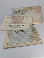 Three folded National Geographic maps stacked: 1947 Canada, Alaska & Greenland map on top; 1954 Northern Europe map in the middle; 1951 Central Europe map at bottom, showing moderate wear and slight discoloration.