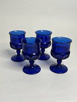 Four cobalt blue glass goblets arranged in a cluster showing their rounded bowls, stems, and bases.