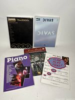Five music books displayed upright and flat, showing covers clearly including Essential Songs The 2000s and VH1 Divas titles.