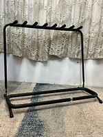 Front angled view of the black foam padded folding rack for guitars and basses, showing the base and seven foam-padded supports on the top bar.