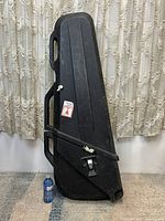 Full front view of black SKB hard plastic electric bass travel case showing overall shape, size compared to water bottle for scale.