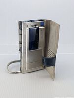 Front view of AIWA TP-M7 micro cassette recorder with flip cover partially open, showing the device's screen and speaker grille.