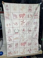 Full front view of entire quilt hanging showing all 35 embroidered squares in grid formation with red stitching and some beige.