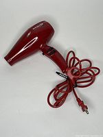 Full view of the red BaByliss PRO Volare V1 hairdryer showing handle, nozzle, and plugged-in red power cord.