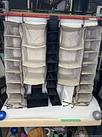 Front view of multiple hanging closet shelves including beige fabric organizers with multiple compartments and a narrow black hanging organizer in the center.