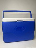 Front view of the medium-sized Coleman cooler showing the blue body, white lid, and blue swing-up handle.