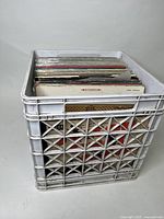 White plastic crate filled with approximately 50 vinyl records showing edges of album covers.