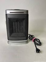 Front view of the rectangular silver and black oscillating ceramic heater with mesh heat vent and power cord coiled beside it.