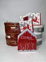 Overall lot with stacked Merry and Bright dessert plates, stacked gray and white penguin dessert plates, Christmas-themed napkins, and Christmas cookie cutters tin