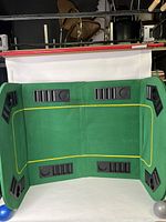 Folded green felt poker table with 8 player positions featuring black cup holders and chip trays, showing yellow border lines on felt surface.