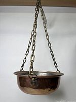 Copper hanging plant pot suspended by three brass-colored chains shown from side with visible patina and surface wear.