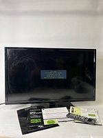 Front view of Insignia 32 inch LED TV powered on with 'No Signal' message displayed, showing screen and included printed user manuals and remote in front.