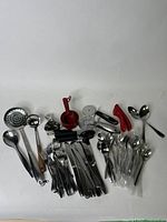 Top-down view of assorted kitchen utensils on white surface, including cutlery, measuring cups, and kitchen gadgets.
