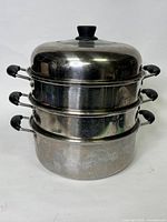 Stacked two-tier stainless steel steaming pot with black handles and matching lid, viewed from the side showing all components stacked together.