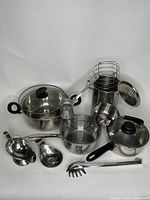 Full set of stainless steel pots and accessories including lids, basket, gravy boat, and ladle arranged on white background