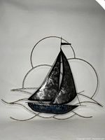 Full front view of dark metal sailboat wall art with circular arcs representing sunset and clouds, against a white background.