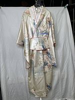 Full view of cream colored kimono with peacock and floral prints hanging against white sheet background
