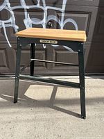 Right side angle view of Shop Fox work table showing solid wood top, black steel frame, and adjustable feet.