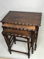 Front angled view of all three nesting tables stacked showing scalloped edges and turned legs.