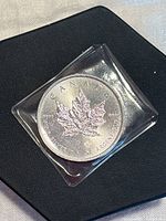 2014 Canada Silver Maple Leaf bullion coin in protective plastic sleeve on a dark surface, showing the full map leaf design and inscriptions.