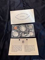 Top view showing coins in sealed plastic set with original envelope and certificate below on black fabric background.