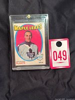 Front view of the vintage Jacques Plante hockey card from 1971-72 O-Pee-Chee series, displayed in a plastic holder with a lot number card beside it.