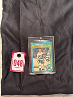 Original photo shows the card encased in plastic with auction tag number 048 next to it for identification.