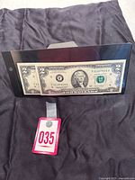 Two consecutive 2003 $2 bills in protective display showing serial numbers.