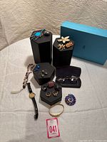 Overview photo showing all jewelry items arranged on table including watch, rings, necklaces, brooches, earrings, bracelet, glasses, and mandala piece.