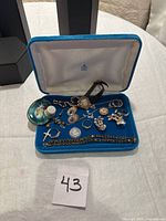 Open blue velvet pouch with assorted jewelry on fabric backdrop