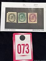 Set of three vintage Victorian Canadian stamps on black card, colors black, green, and purple, displayed with lot number tag.